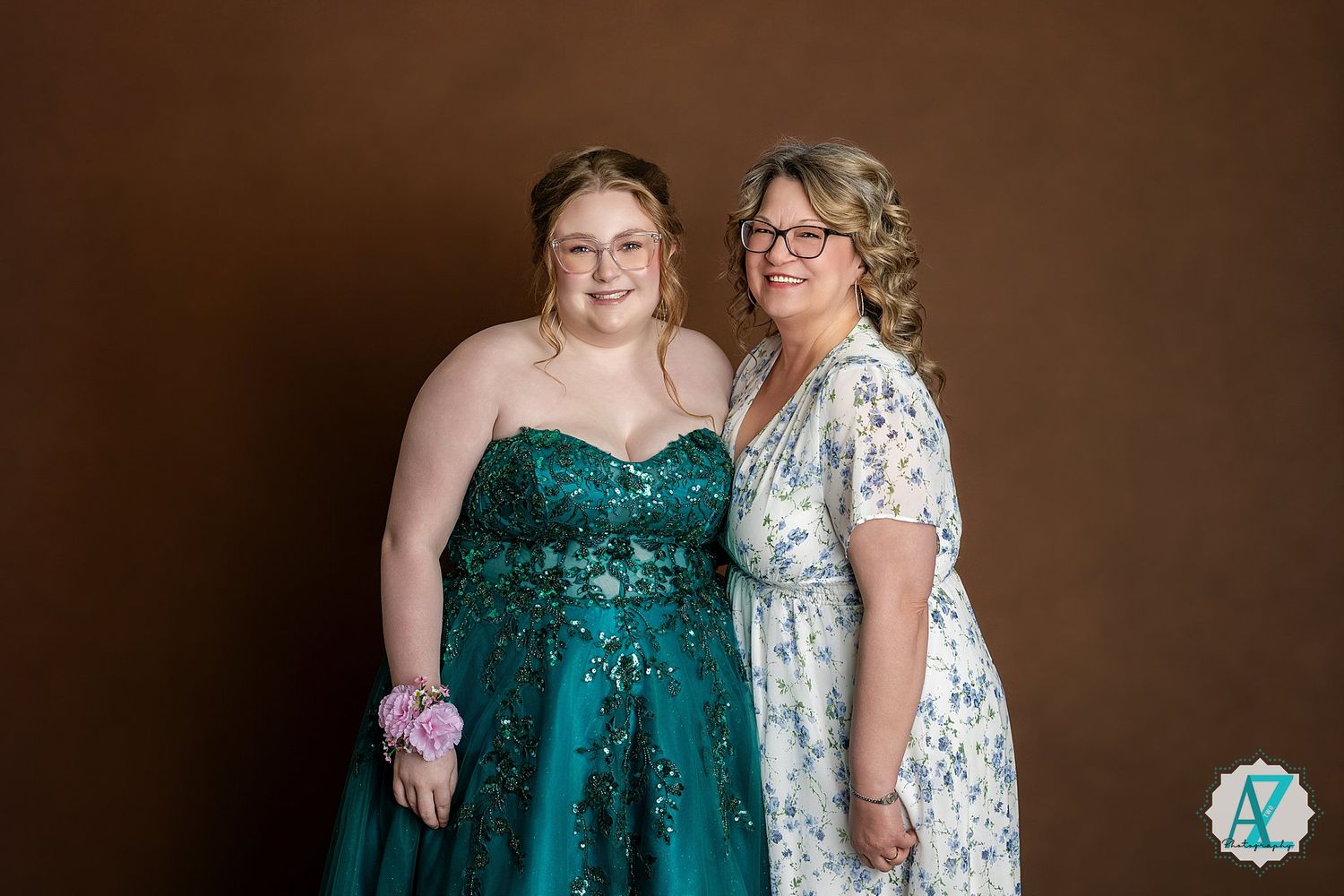 Two people pose together at a formal event wearing a teal sequined gown and a white floral dress.