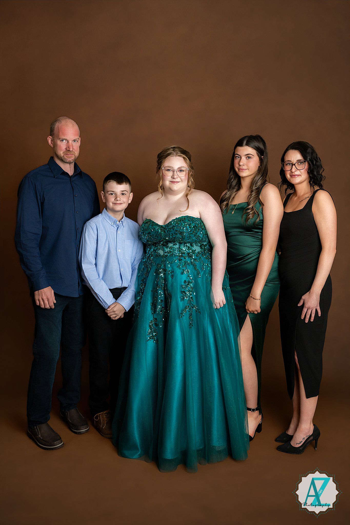 A formal family portrait against a brown backdrop featuring five people with one wearing a sparkling emerald gown.