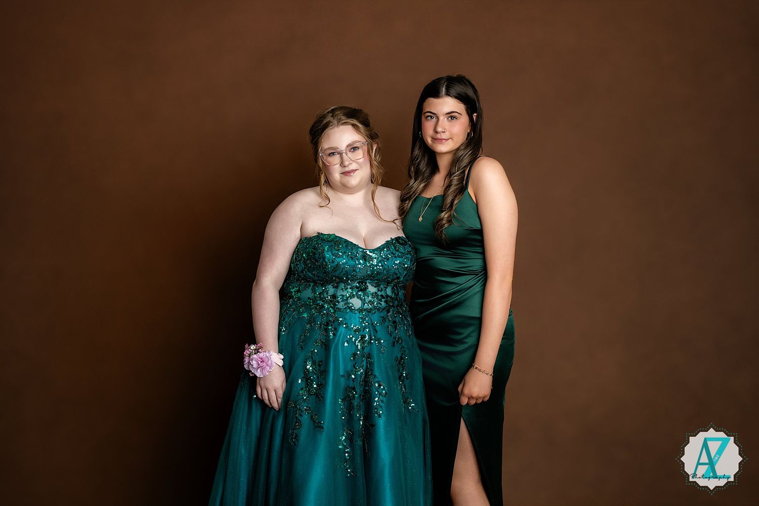 Studio portrait features two people in coordinating emerald green formal wear against brown backdrop.