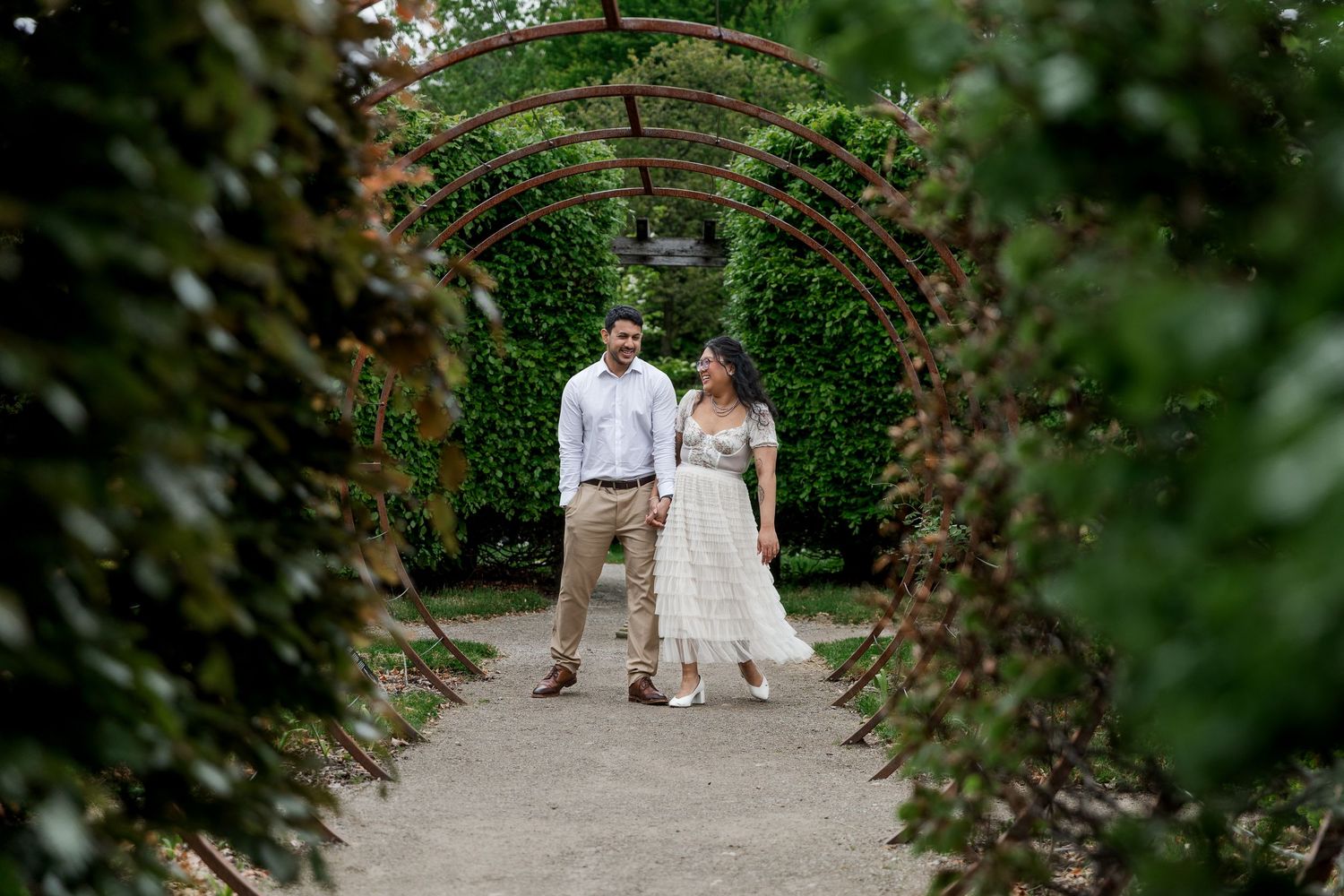 Candid engagement photo of couple bumping hips and laughing through the gardens at the Guelph Arboretum in Guelph, Ontario.
