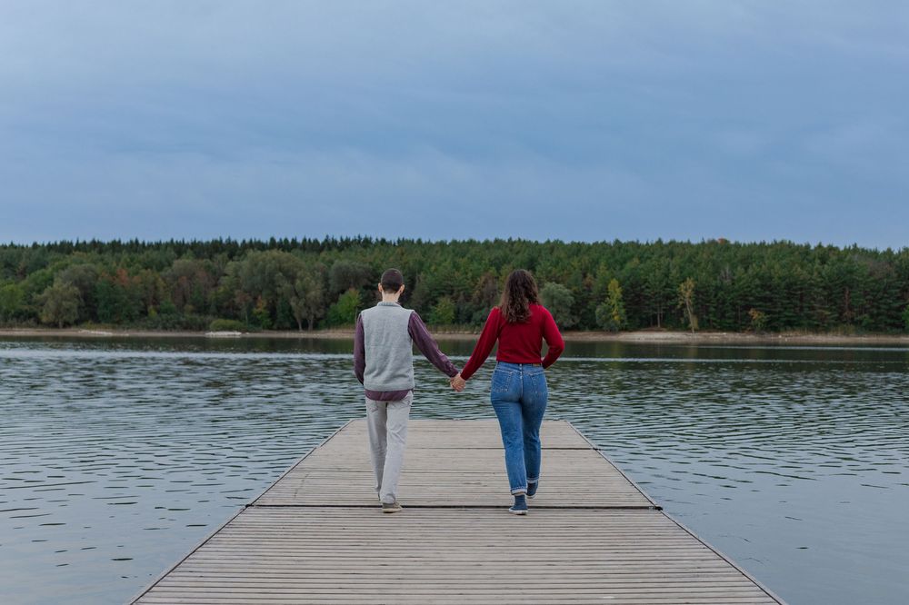 Candid engagement photo of couple holding hands walking on a dock at the guelph lake conservation area in guelph, ontario.