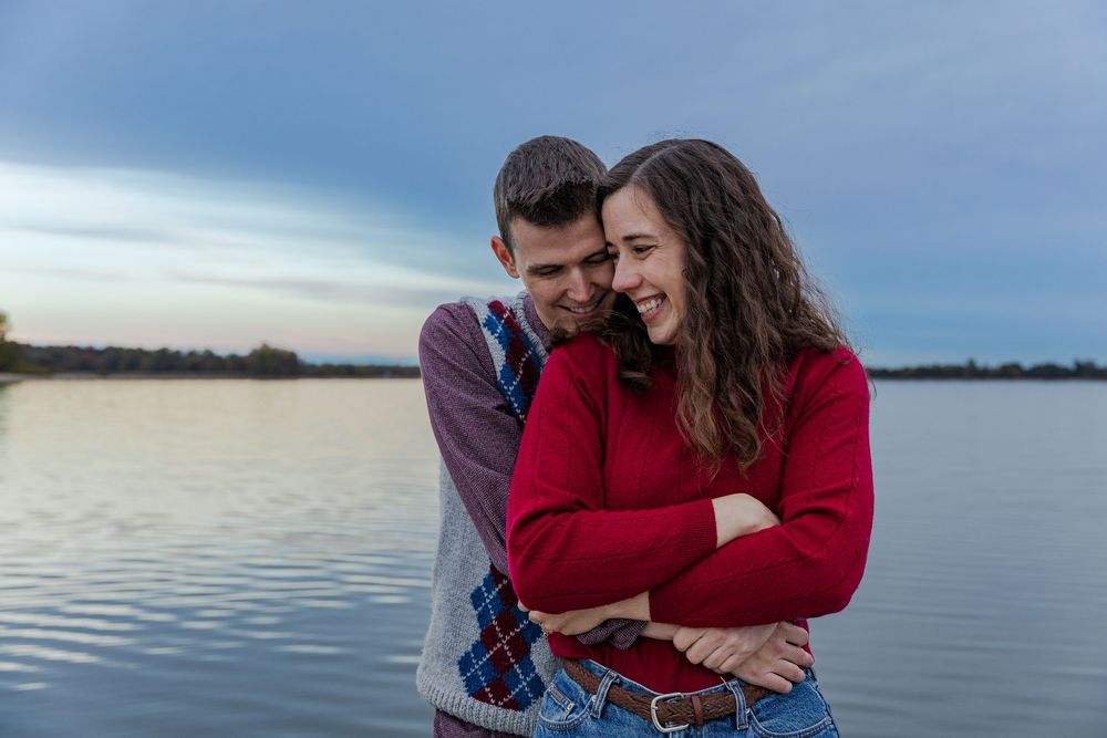 Couple embracing during their sunset engagement session by the water at the guelph lake conservation area in guelph, ontairo.