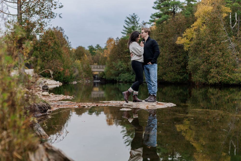 Natural engagement photo of couple snuggling close together over the water at the rockwood conservation area in rockwood, ontario.