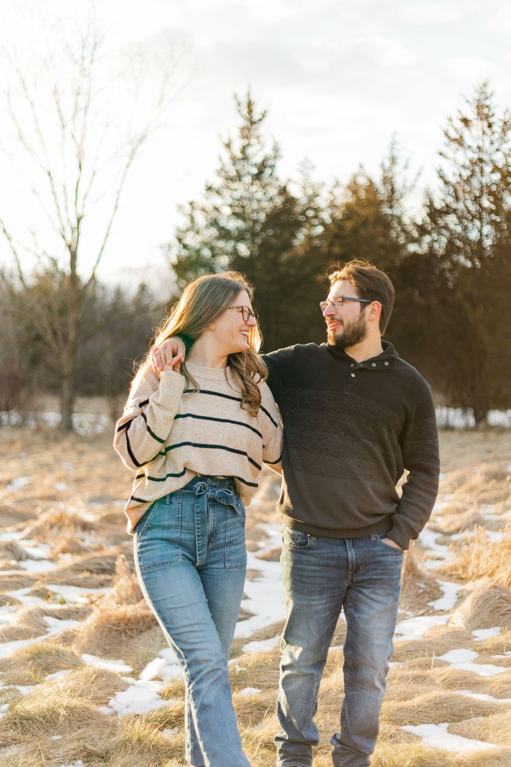 Couple walking together in a field during sunset at their winter engagement session at the guelph arboretum in guelph, ontario.
