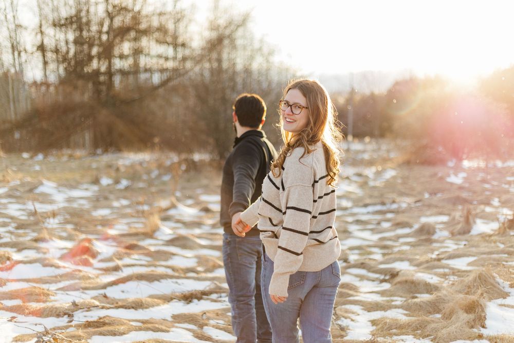 Relaxed engagement photo of couple walking through a field at sunset during winter engagement session at the guelph arboretum.