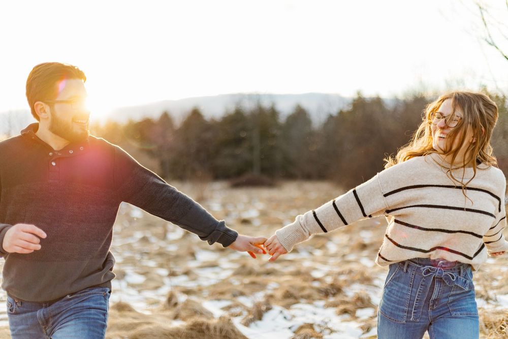 Candid engagement photo of couple running through a field during sunset in their winter engagement session at the guelph arboretum.