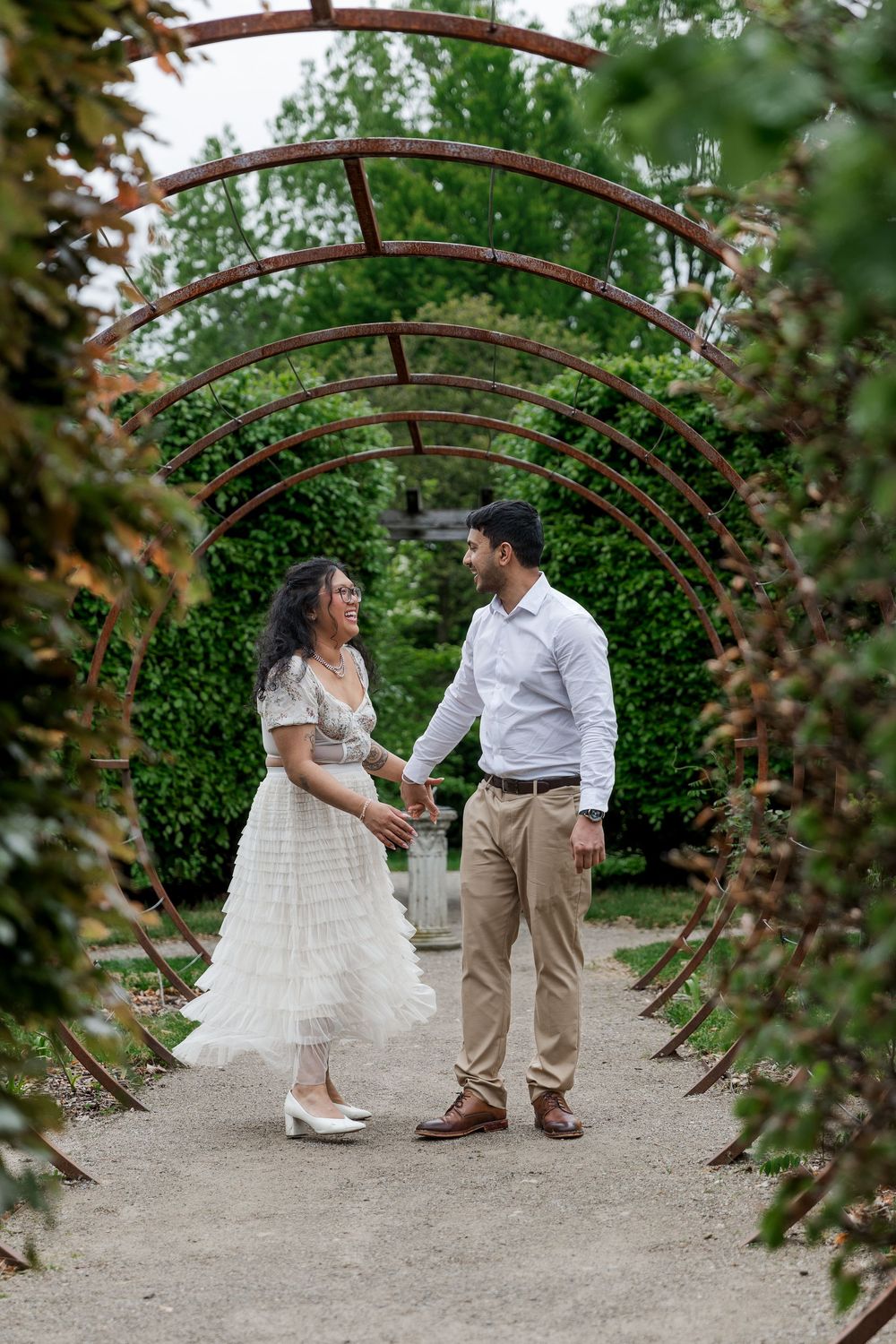 Candid engagement photo of couple walking through an art piece in the gardens of the Guelph arboretum in Guelph, Ontario