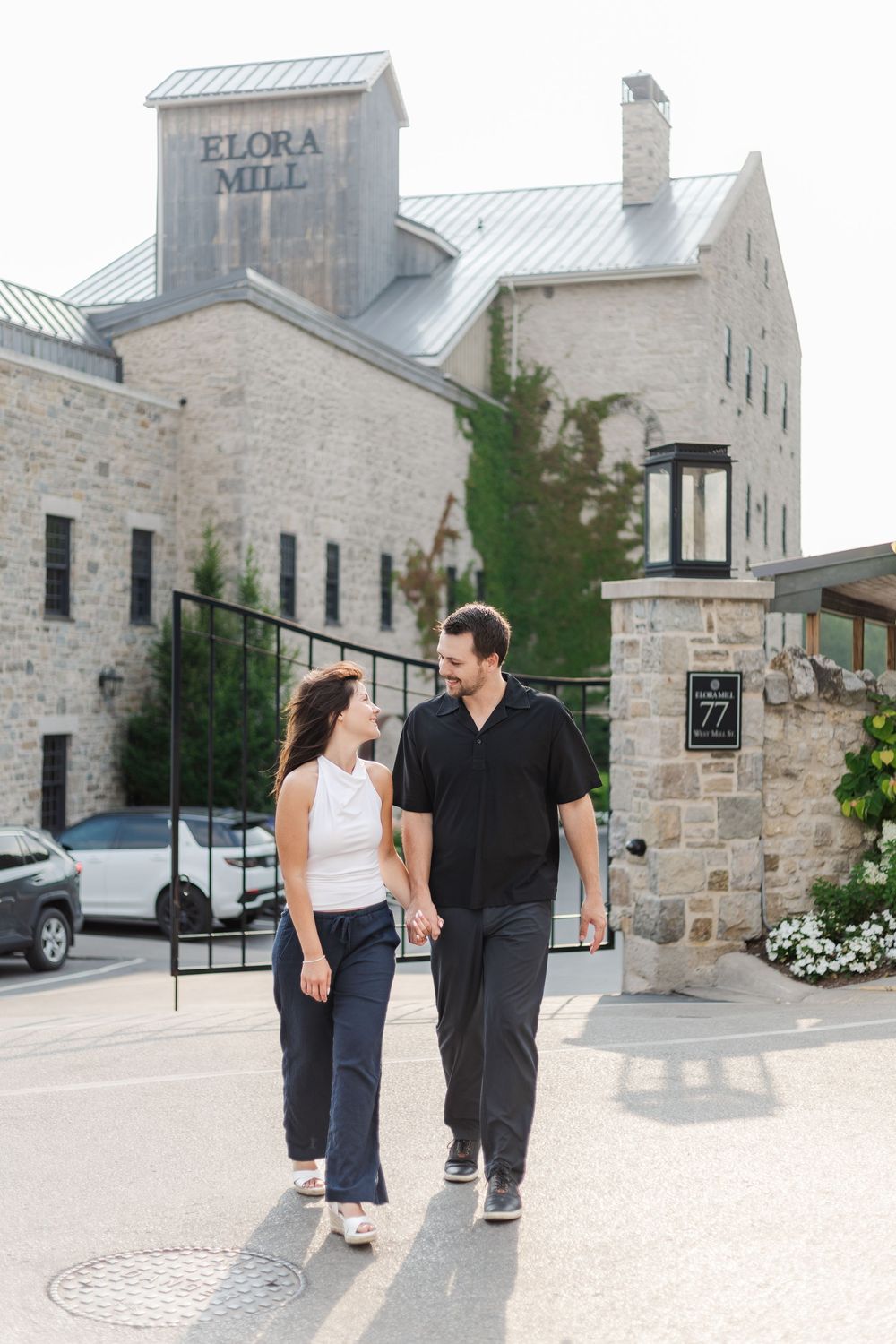 Natural engagement photo of couple walking together across the street of the Elora mill in downtown Elora, Ontario