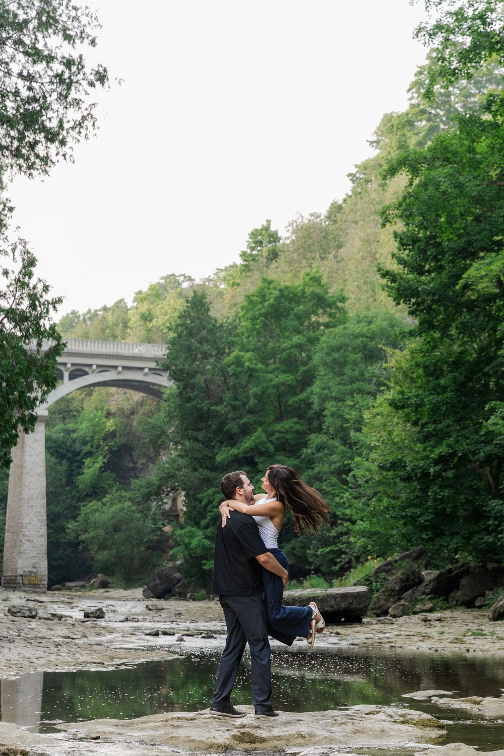Candid engagement photo of couple spinning in the river bed of the elora gorge in downtown elora, ontario.