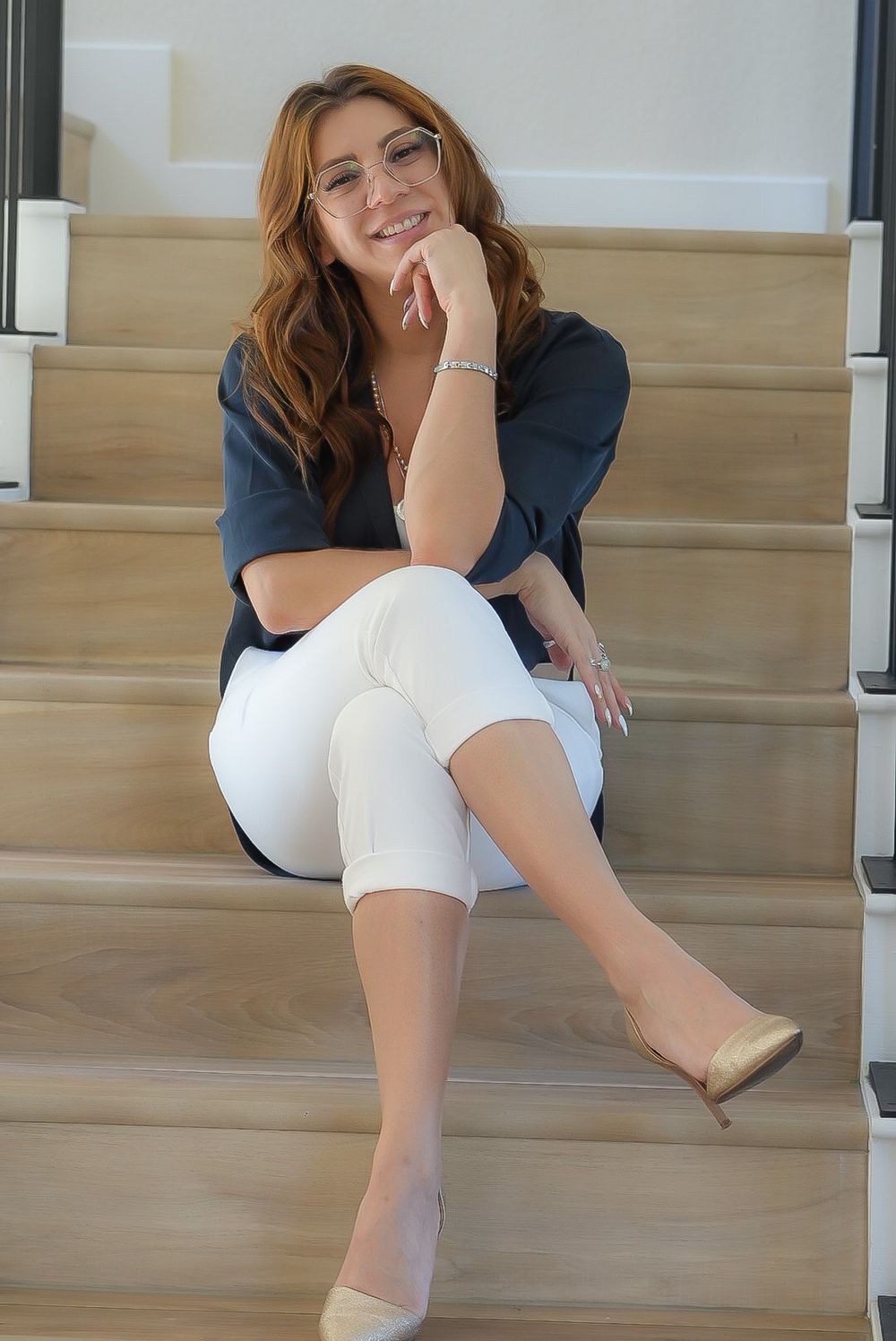 Smiling woman with glasses in navy blouse and white pants sitting on stairs.