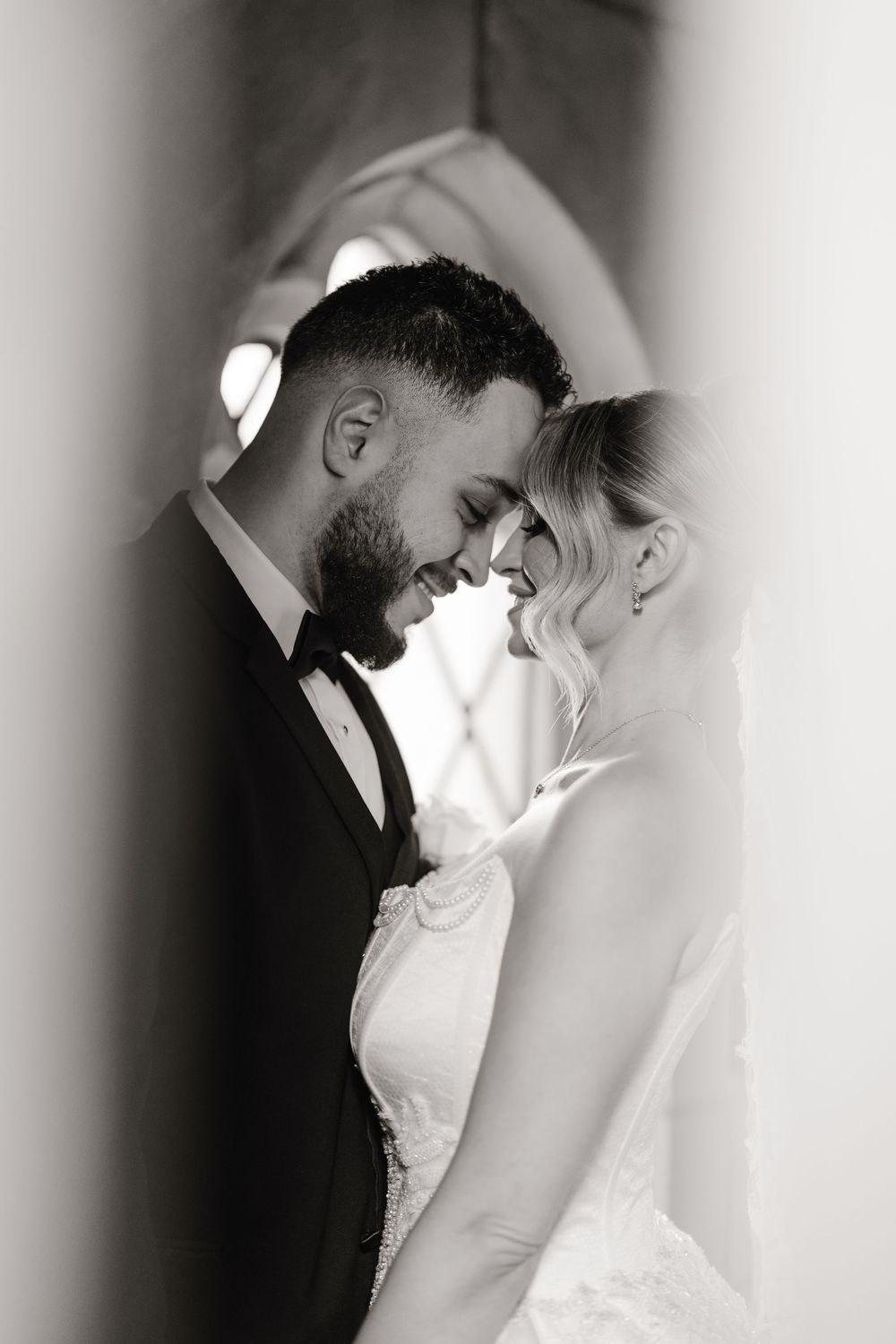 Black and white portrait of bride and groom touching foreheads tenderly in a romantic wedding moment.