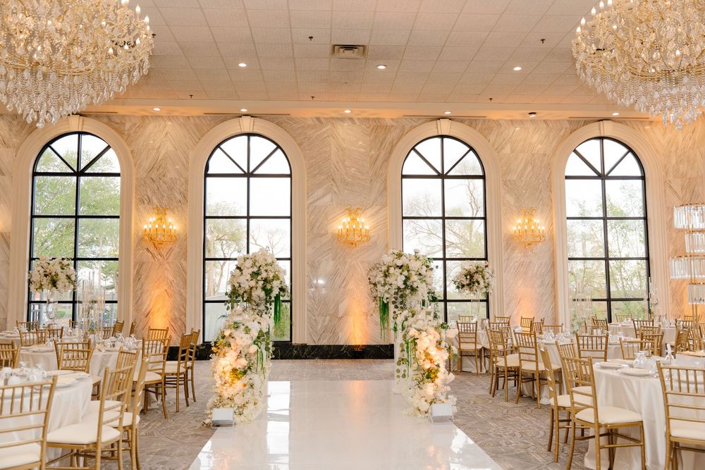 Elegant wedding reception hall with crystal chandeliers, gold chiavari chairs, and floral arrangements on a white dance floor.