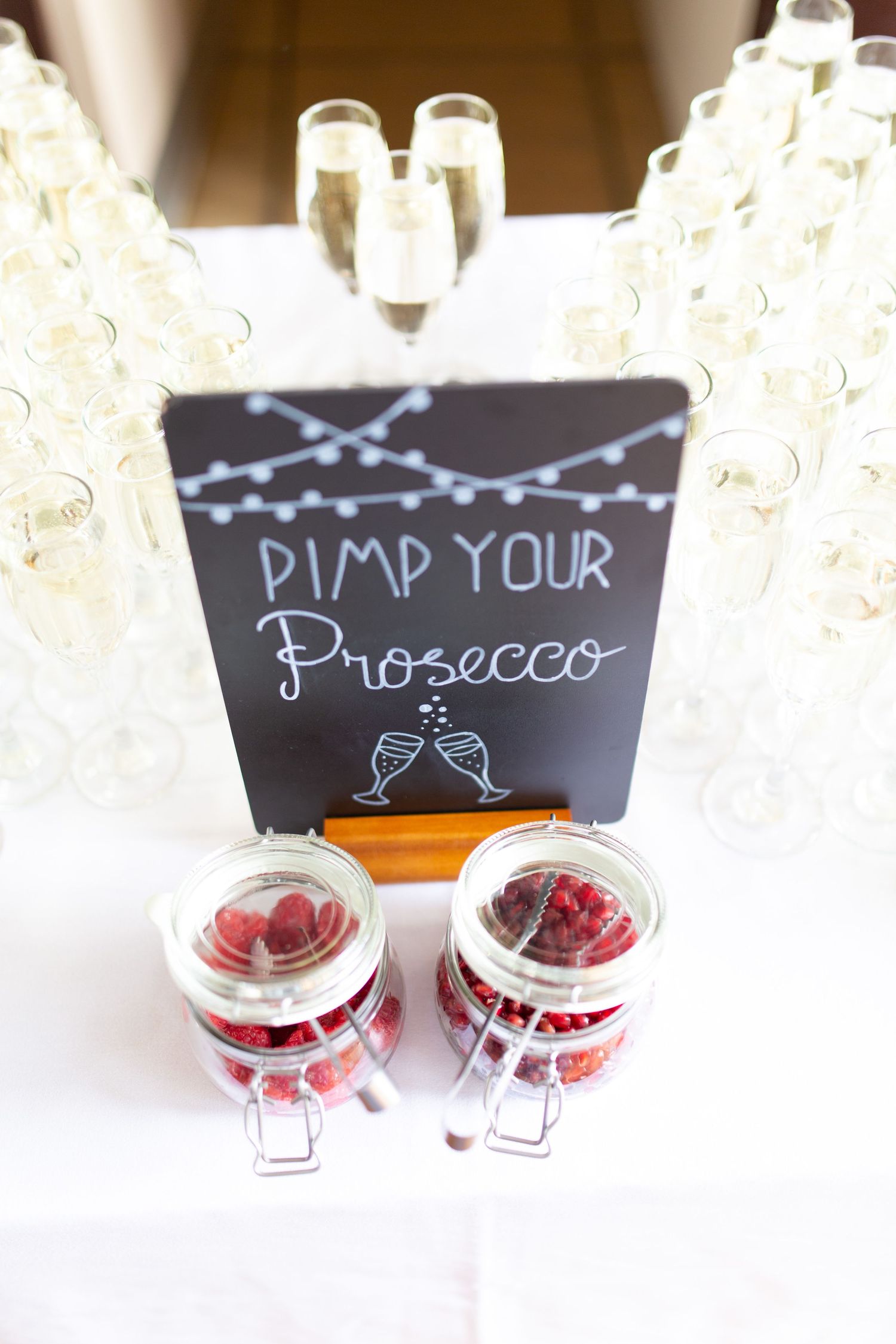 Pimp Your Prosecco bar with champagne flutes and jars of fresh raspberries on a white table.