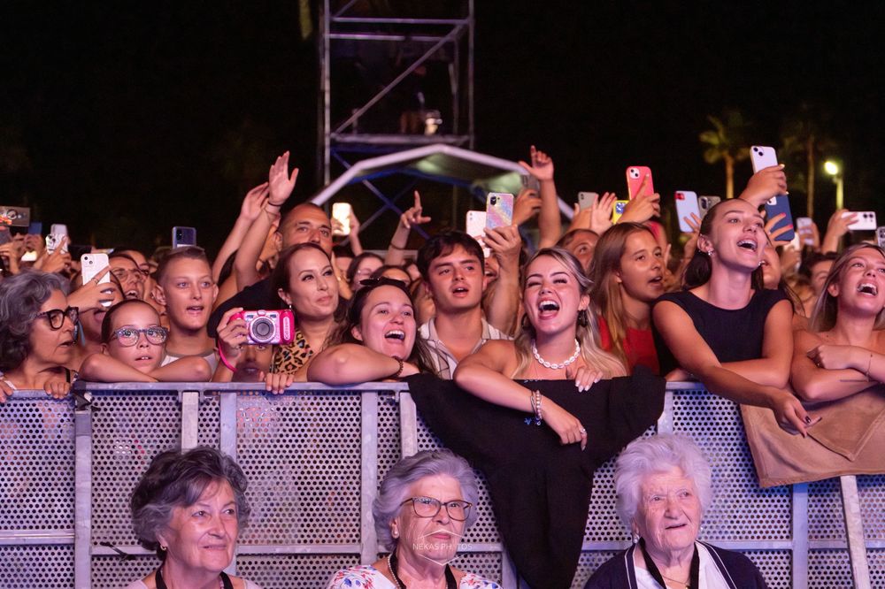 Excited crowd of fans cheering and taking photos at an outdoor concert at night.