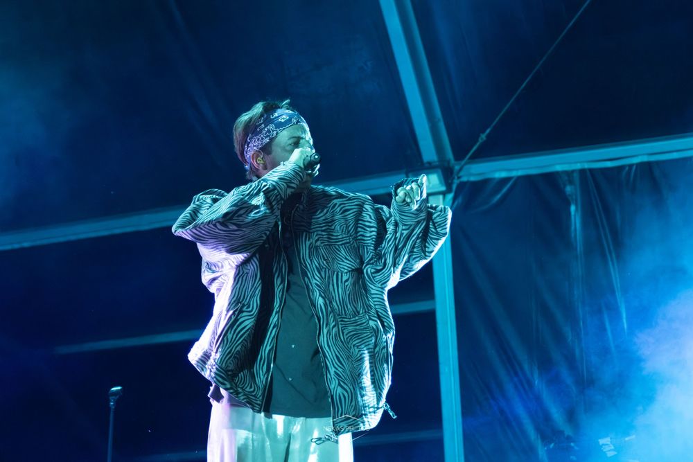Singer performing on stage under blue stage lights, wearing an oversized jacket and white pants at a live concert.