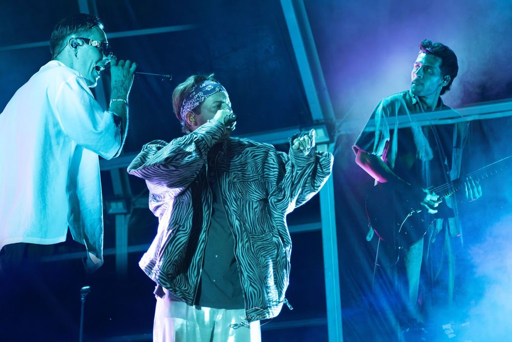 Three performers on stage bathed in blue and purple lighting during a live music concert performance.