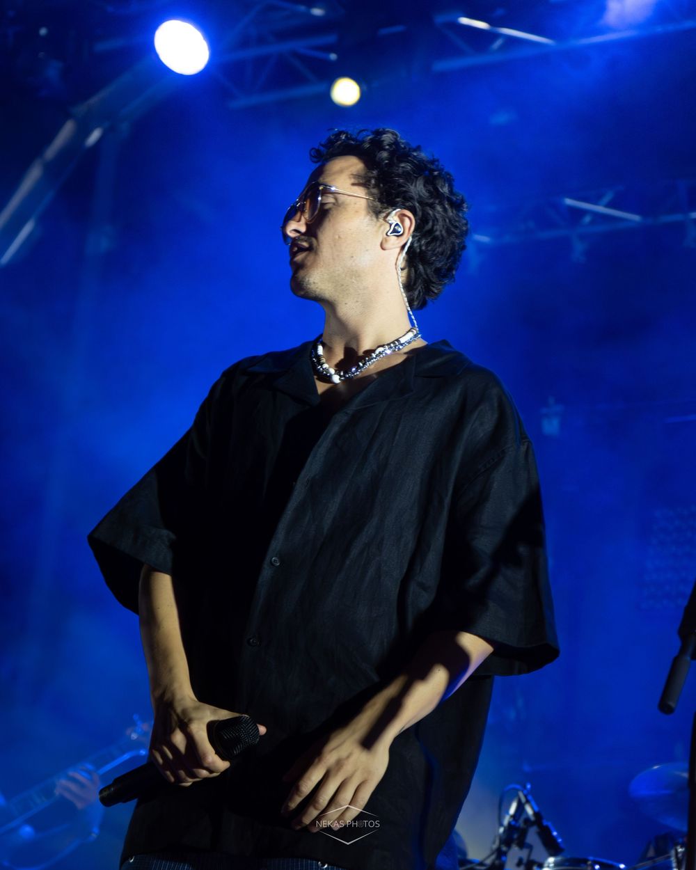 Performer in black outfit holding microphone on stage with blue lighting at live concert.