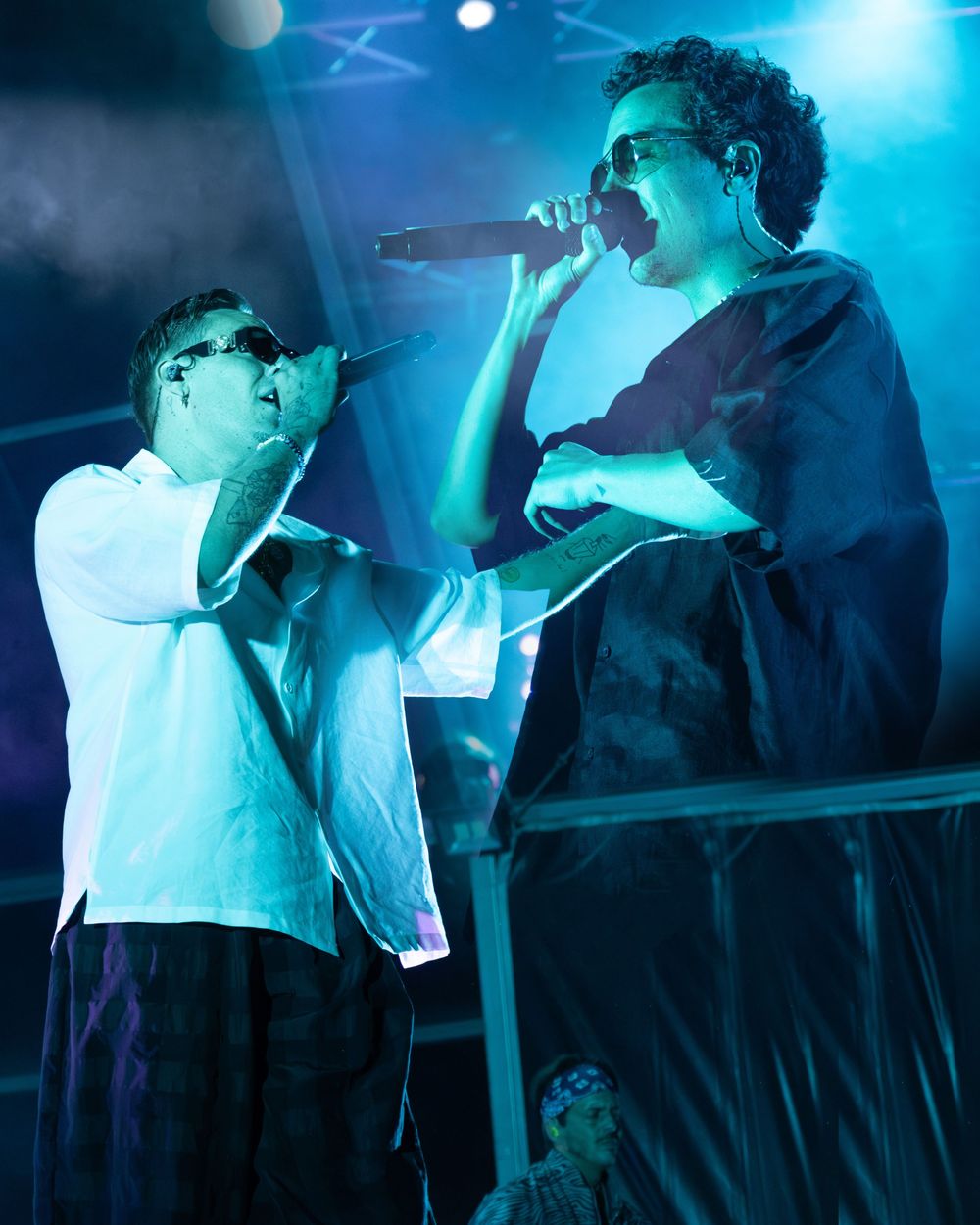 Two male performers singing into microphones on a blue-lit stage during a live concert performance.