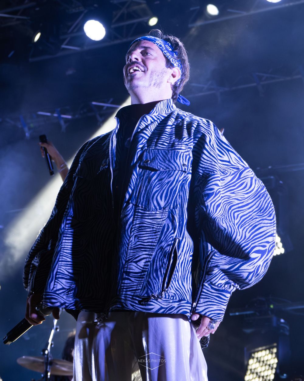 A performer in a blue zebra-print jacket and headband sings on a lit stage.