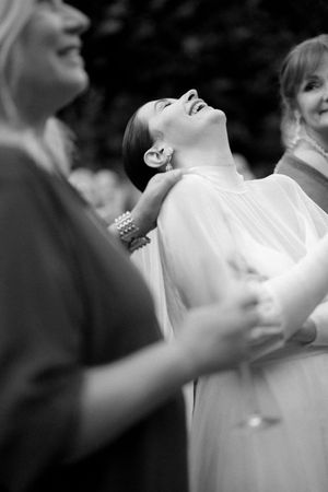 Bride laughing joyfully in a white gown surrounded by guests at an outdoor wedding reception.