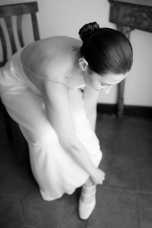 Bride in white gown adjusting her shoe, captured in elegant black and white photography from above.