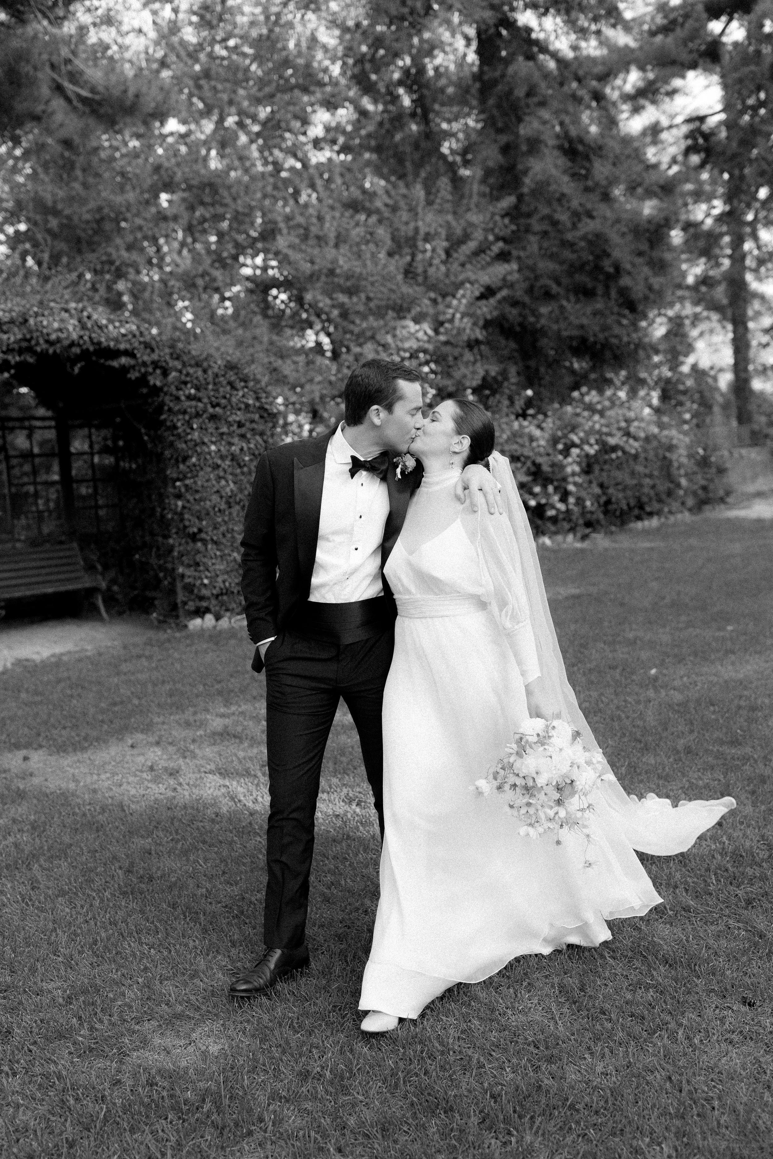 Black and white photo of a bride and groom sharing a kiss outdoors on their wedding day.
