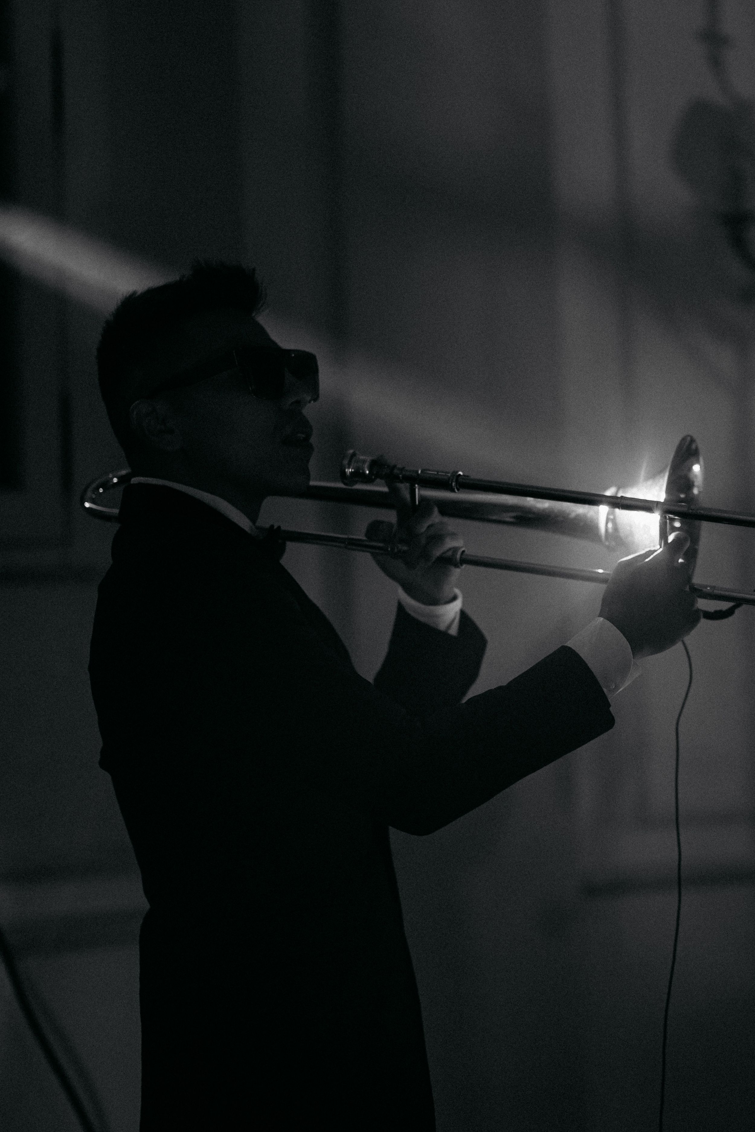 Black and white silhouette of a trumpet player in a suit performing under a dramatic spotlight beam.