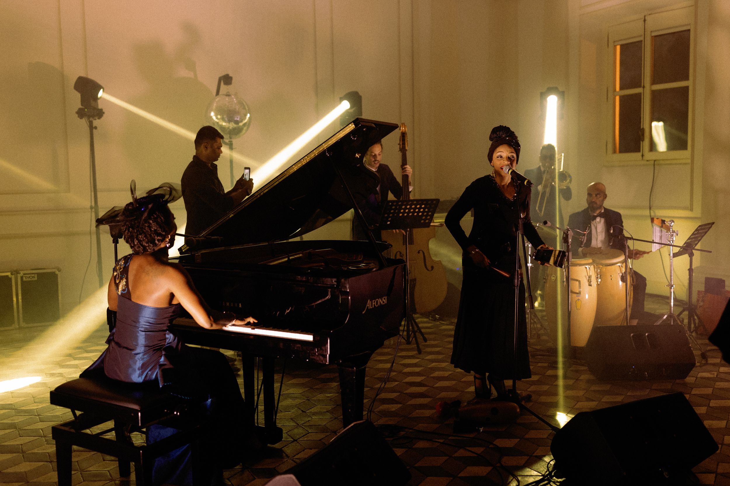 Live jazz band performing in an elegant room with grand piano, vocalist, and warm atmospheric stage lighting.