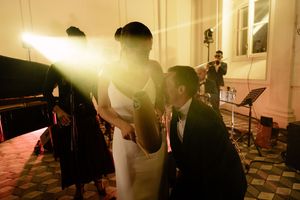 Groom kneeling to kiss bride's hand during romantic indoor wedding ceremony with warm golden lighting.