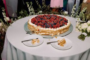 Elegant wedding cake topped with fresh berries displayed on a white linen table with two sliced pieces.