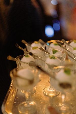 Elegant dessert cups with mint garnish and spoons arranged on a silver tray at wedding reception.