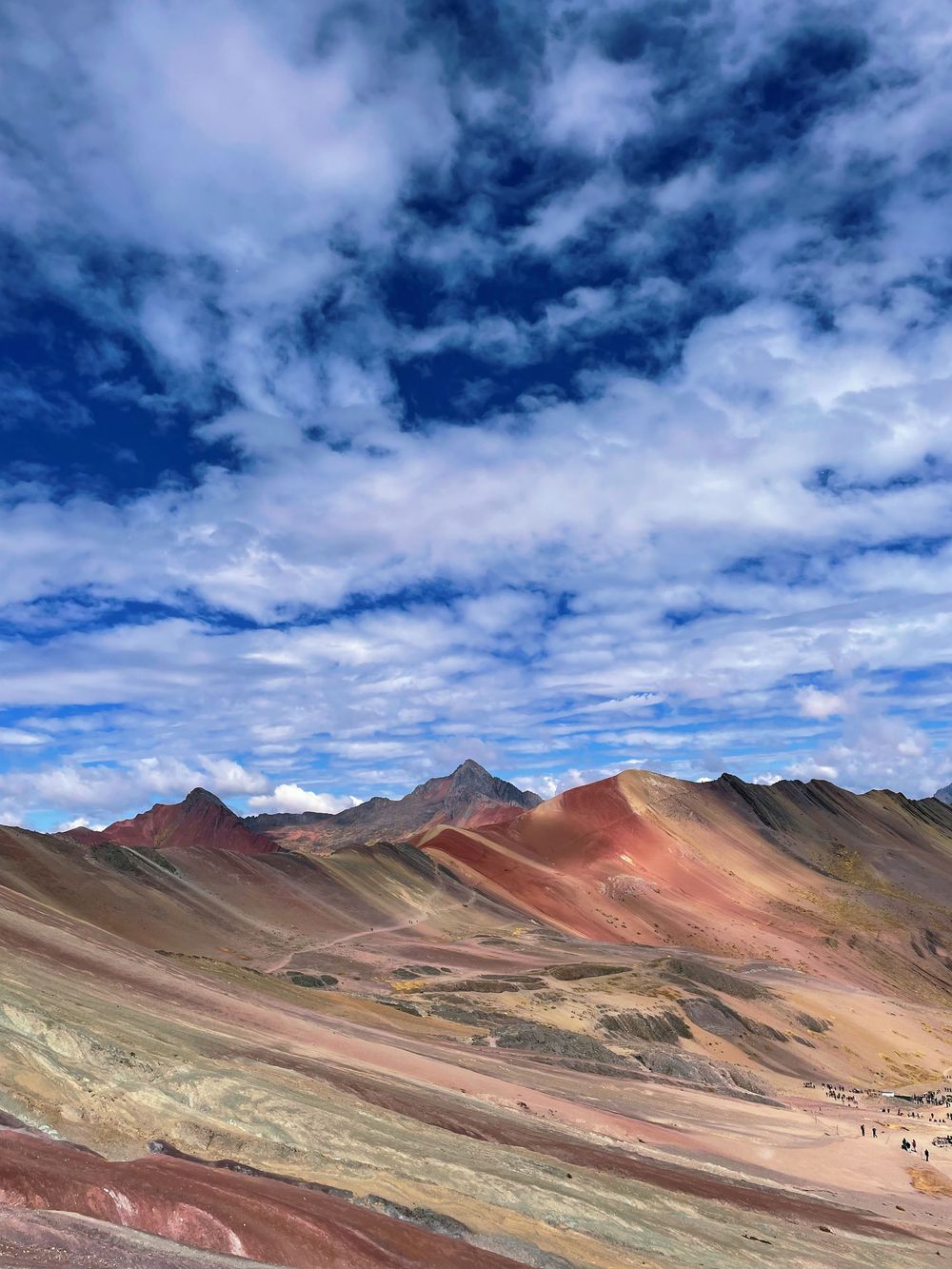 Vinicunca Rainbow Mountain in Peru with colorful mineral-streaked peaks under dramatic blue cloudy sky.