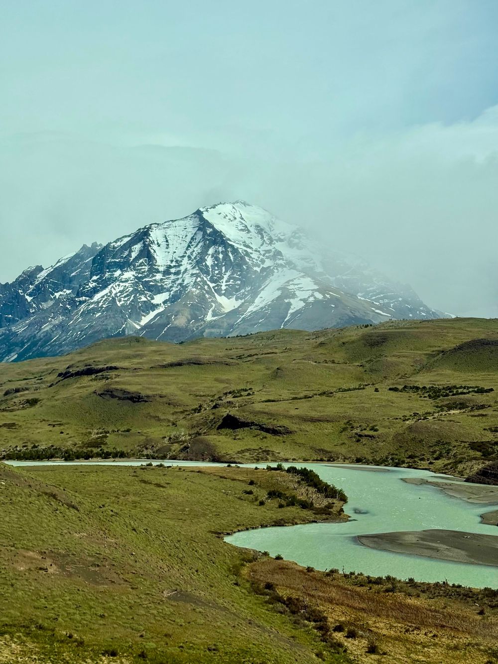 A turquoise glacial river winds through green valleys below a massive snow-capped mountain in Patagonia.