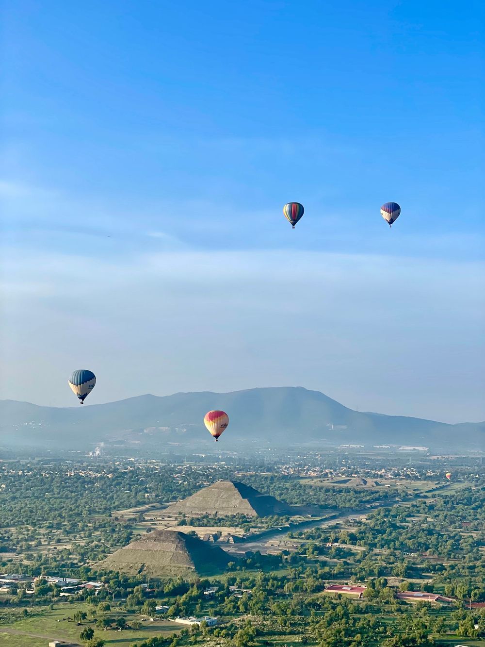 Hot air balloons float above the ancient Pyramid of the Sun at Teotihuacan, Mexico, under a clear blue sky.