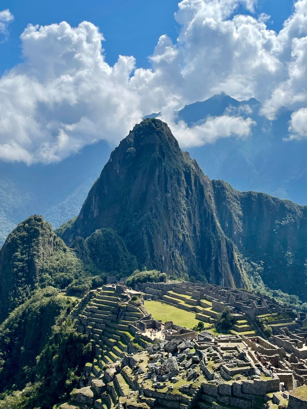 Ancient Inca ruins of Machu Picchu with Huayna Picchu mountain peak rising dramatically under a cloudy blue sky.