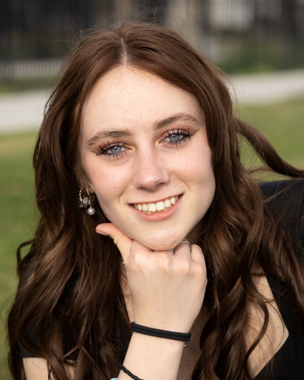 Smiling young woman with long brown hair, blue eyes, freckles, and hoop earrings posing outdoors.