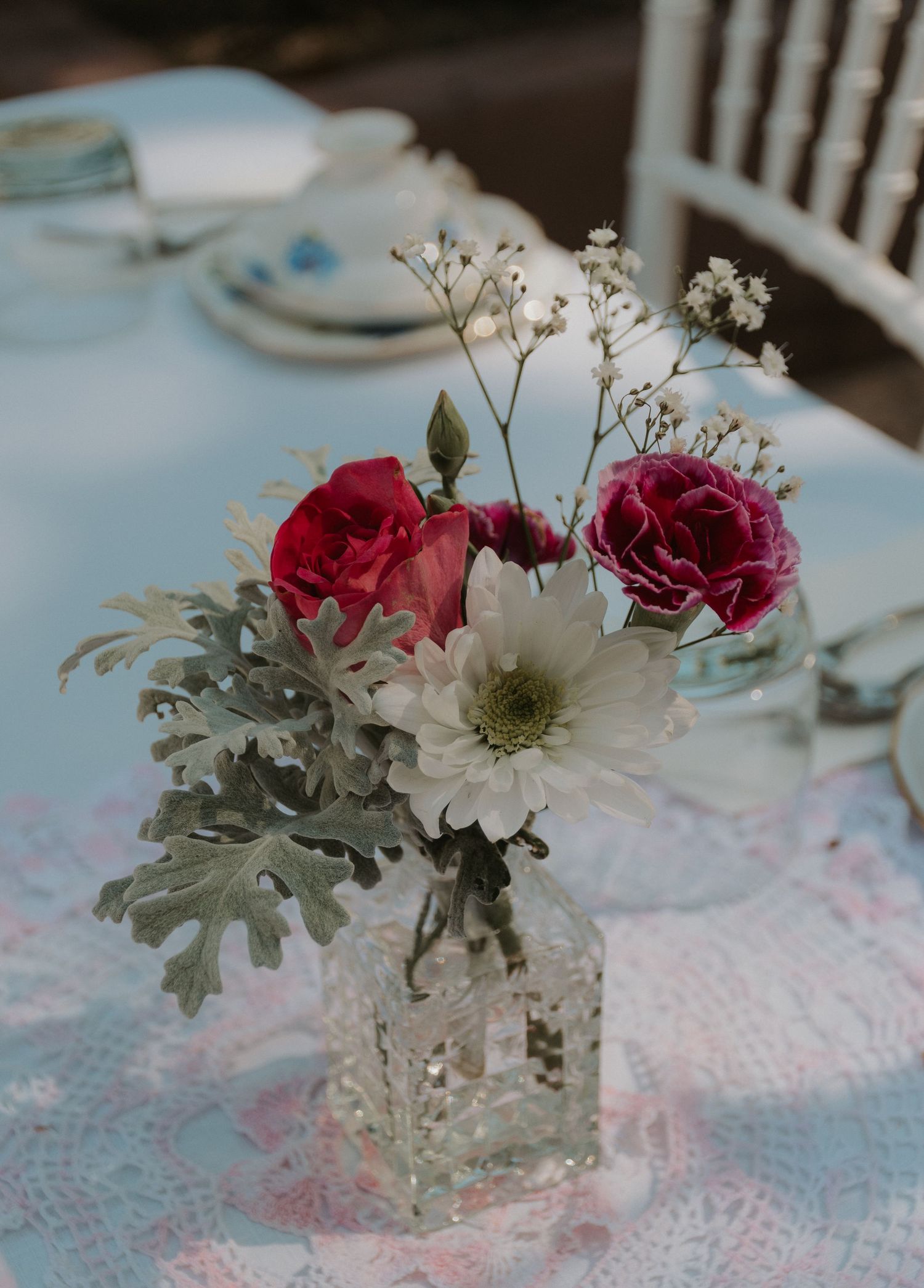 Elegant floral centerpiece with red roses and white daisies in glass vase on white tablecloth.