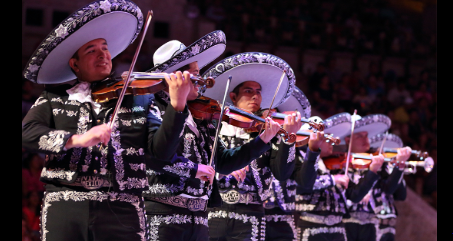 Mariachi band performing in traditional charro suits and sombreros, playing violins on a festive stage.