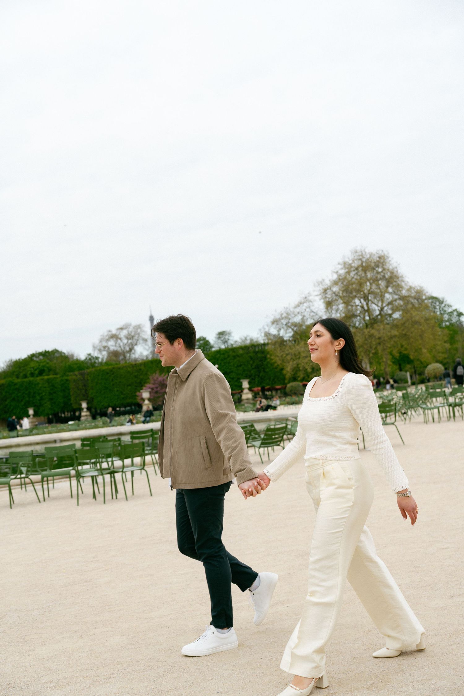 Couple holding hands walking in Tuileries Garden, Paris, woman in white outfit, man in beige jacket. Paris editorial photographer, film