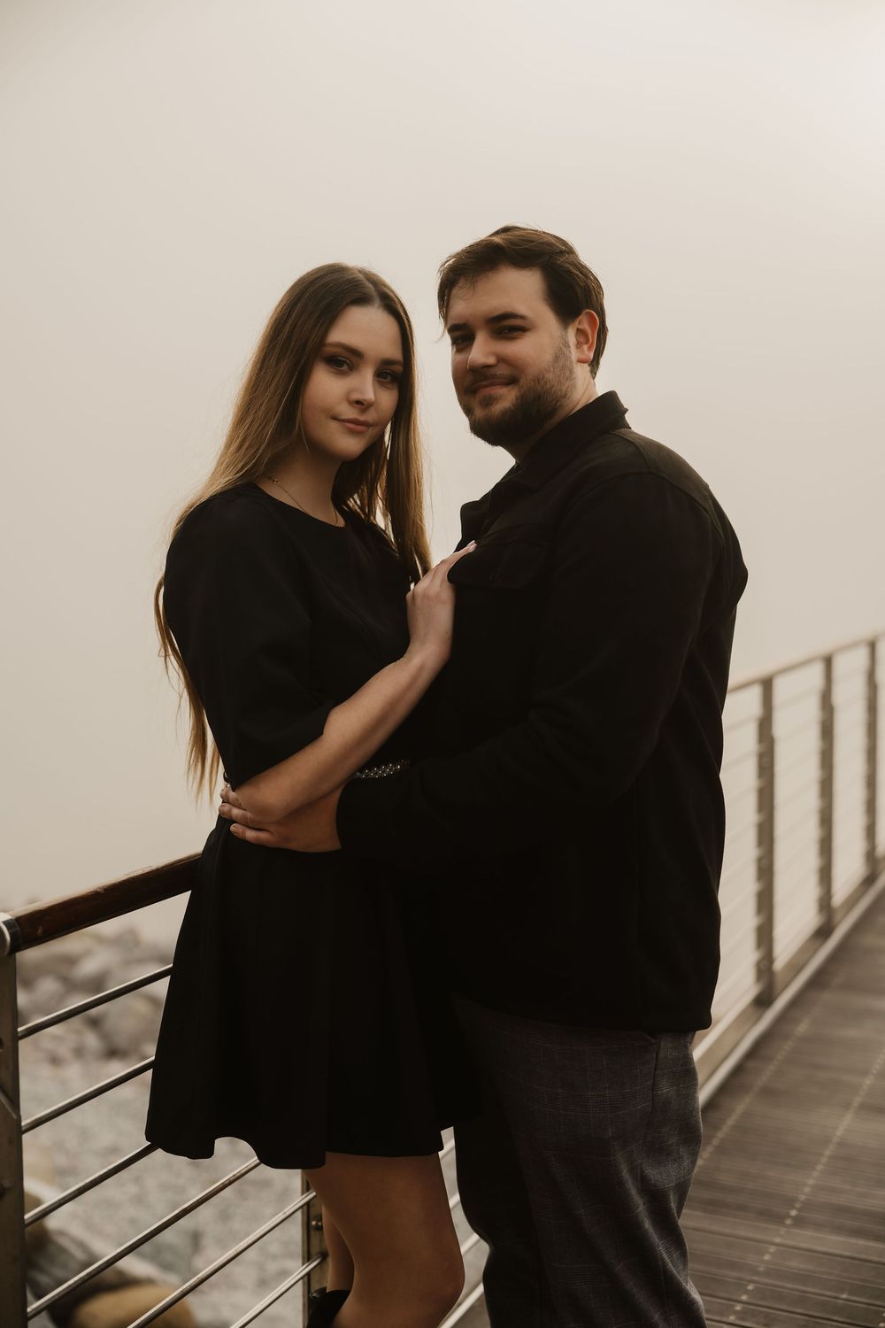 Cinematic pre-wedding photography featuring a couple standing on a cliffside viewpoint in the mist.