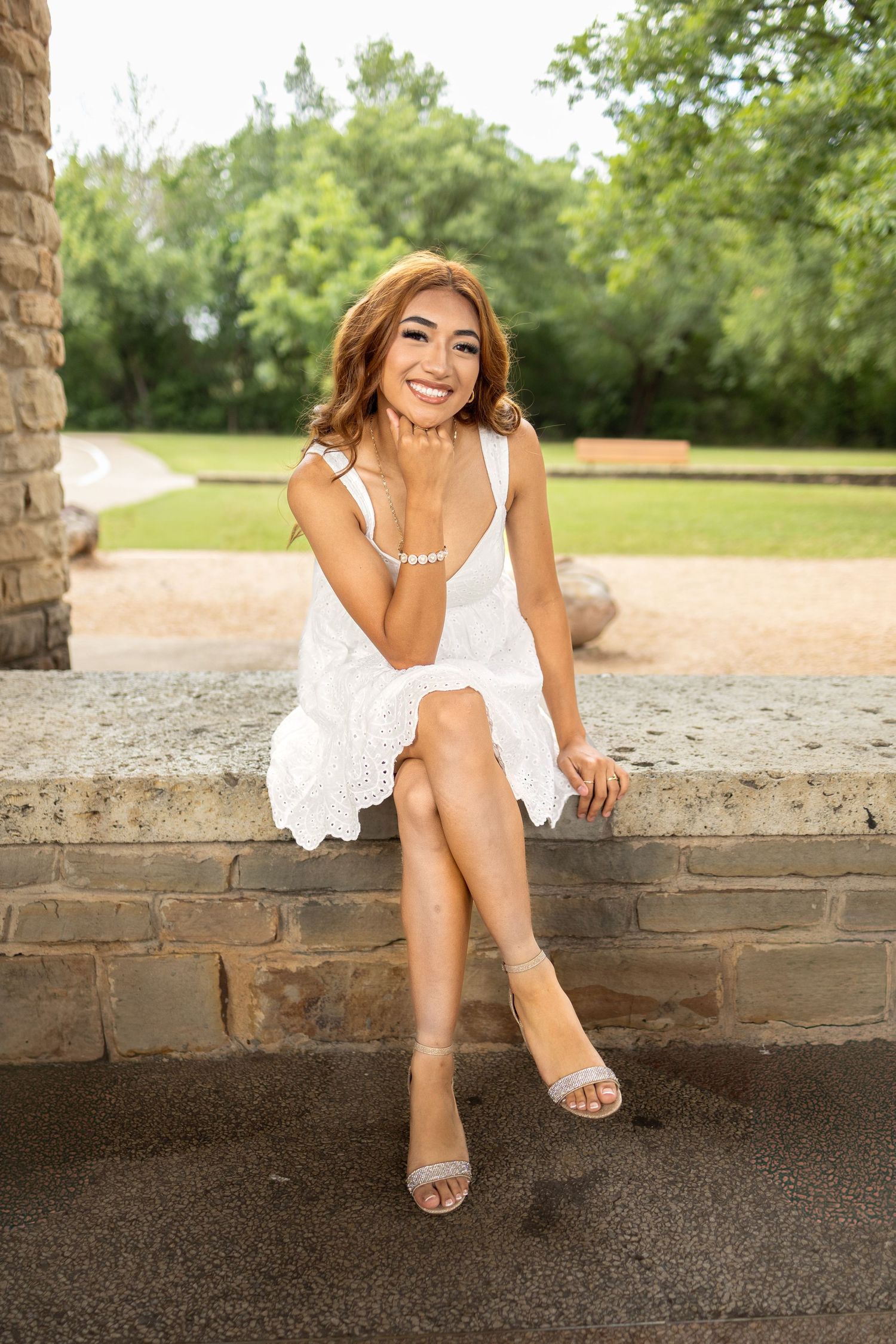Young woman in white dress and white dress sitting on a brick bench smiling