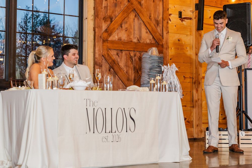Wedding reception toast at The Molloys head table inside a rustic barn venue with wooden doors.