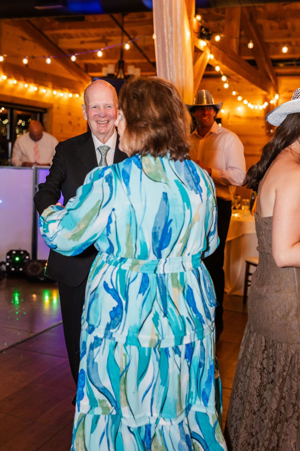 Couple dancing joyfully at a wedding reception in a rustic barn venue with string lights.