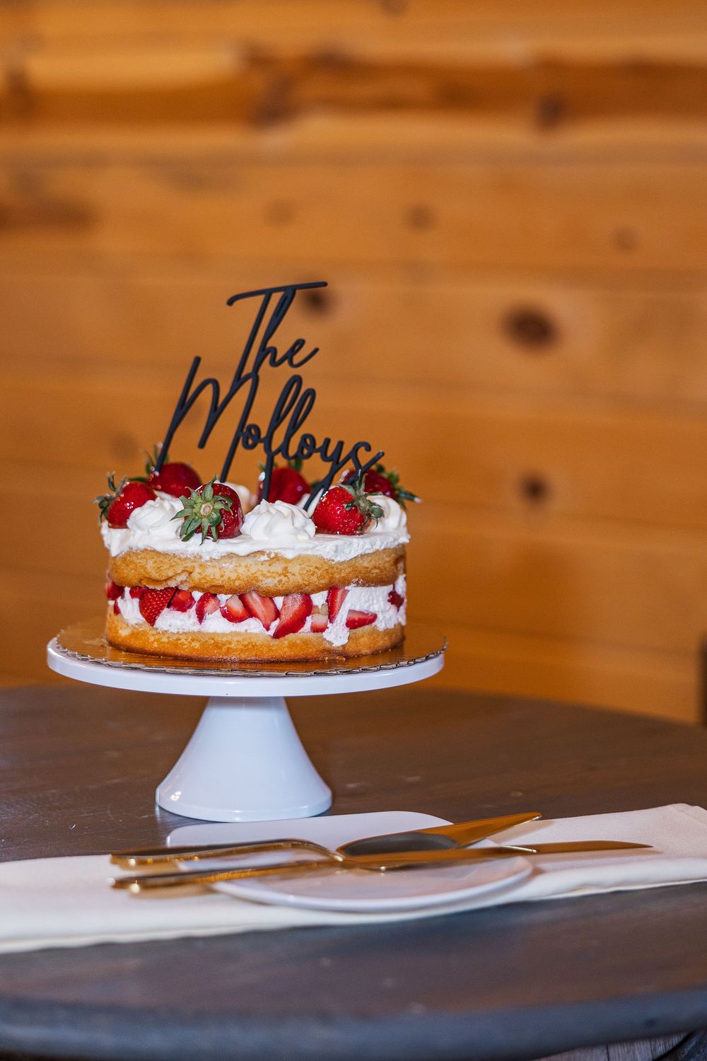 Strawberry shortcake wedding cake with 'The Molloys' topper on white stand, decorated with fresh strawberries and whipped cream.