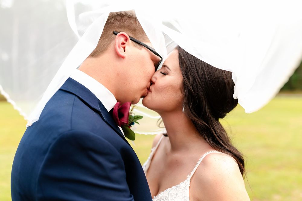 Bride and groom sharing a romantic kiss under a flowing white veil on their wedding day.