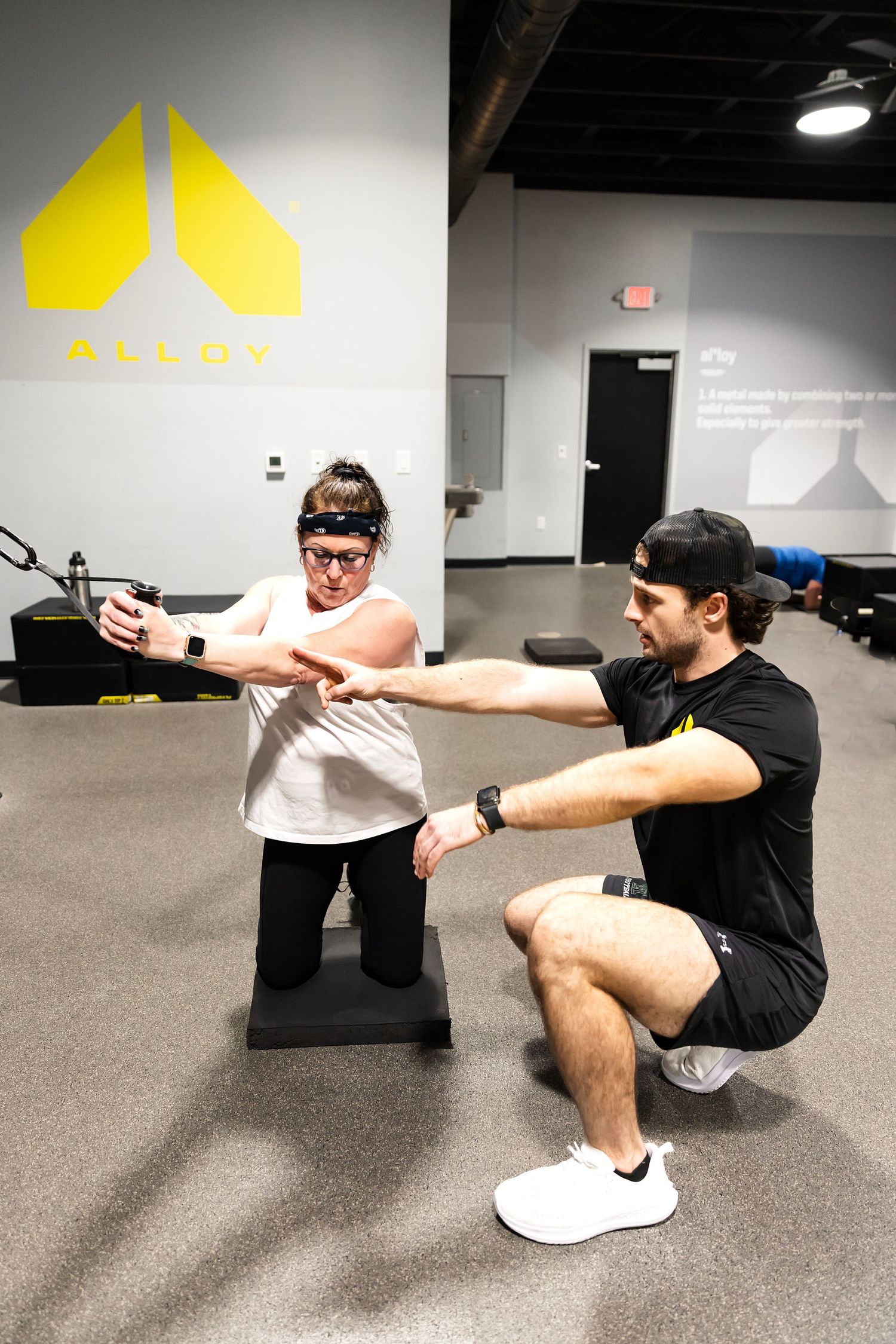 Personal trainer assists a woman with TRX suspension training exercise at Alloy gym facility.