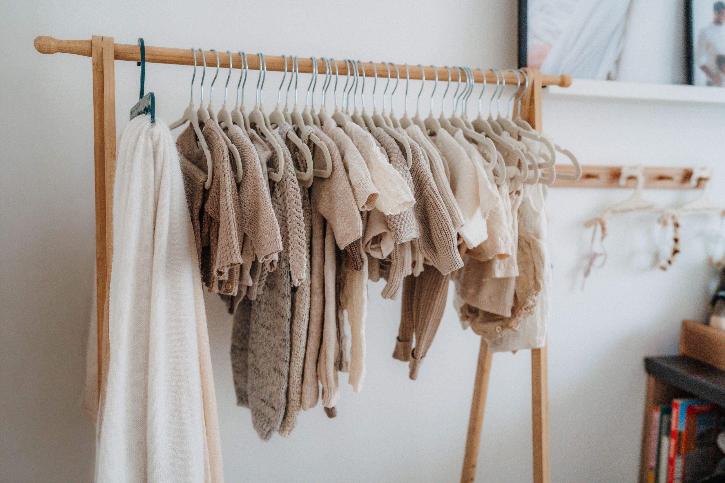 Neutral-toned baby clothes hanging on a wooden clothing rack, featuring beige and cream knit sweaters and tops.