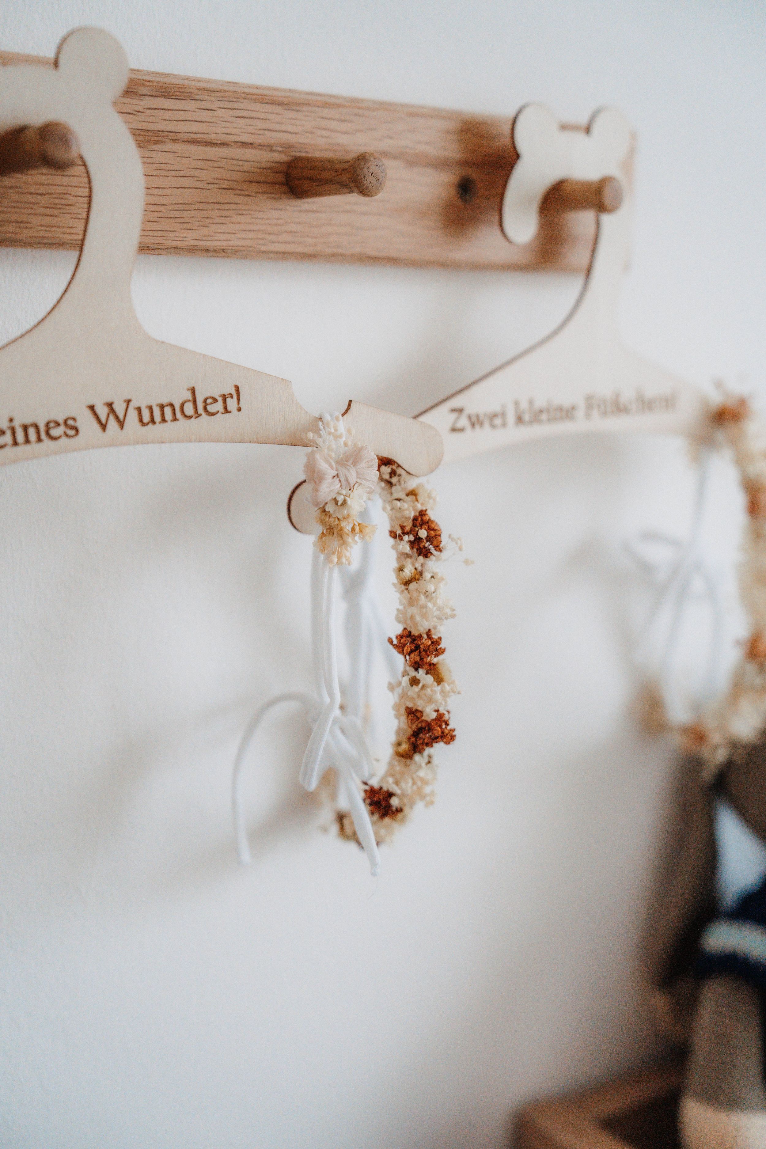 Wooden coat rack with personalized hangers displaying dried flower crowns with white ribbons in a nursery.