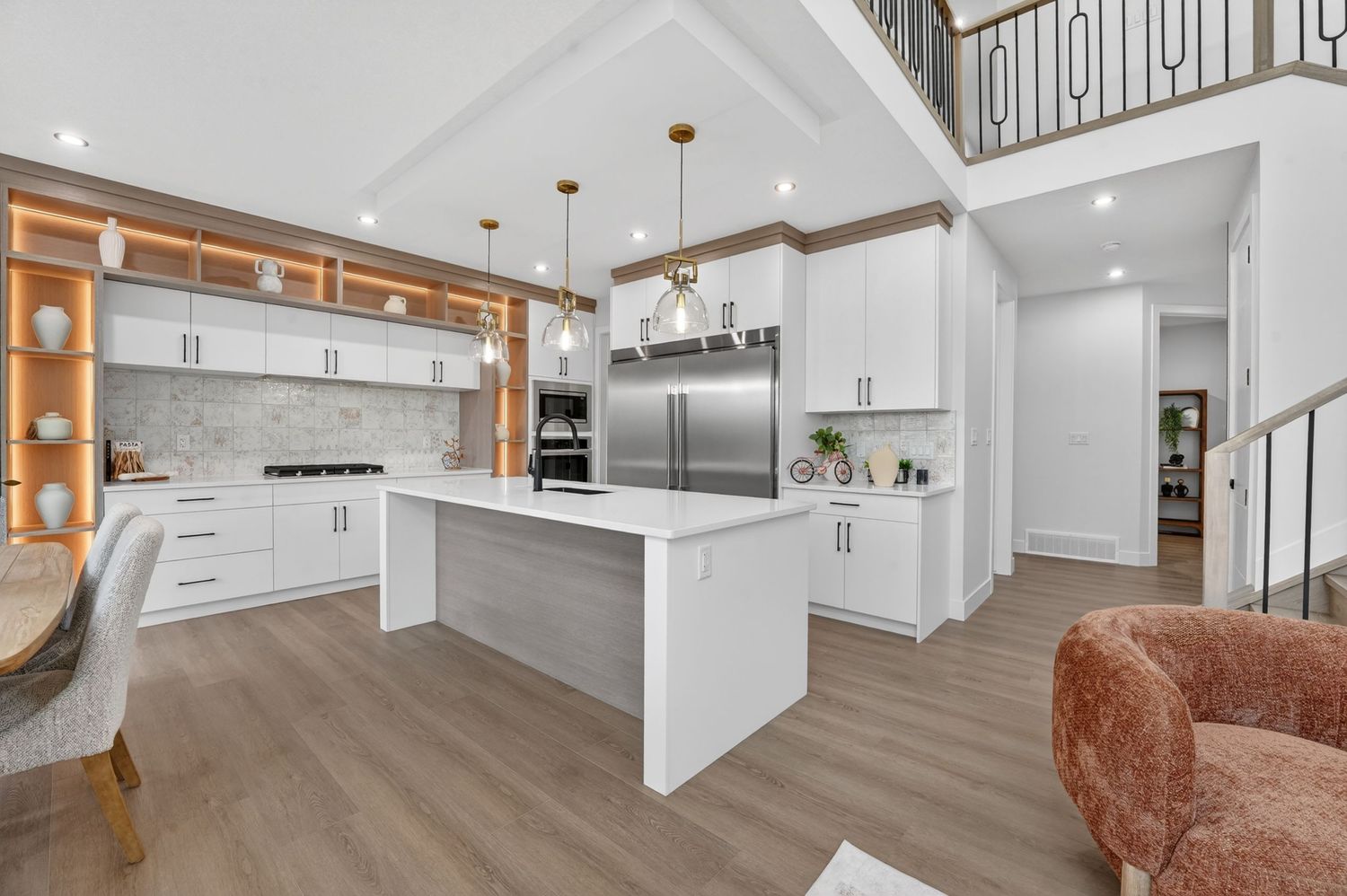 Modern open-concept kitchen with white cabinets, large island, stainless steel fridge, hardwood floors, and elegant pendant lighting.