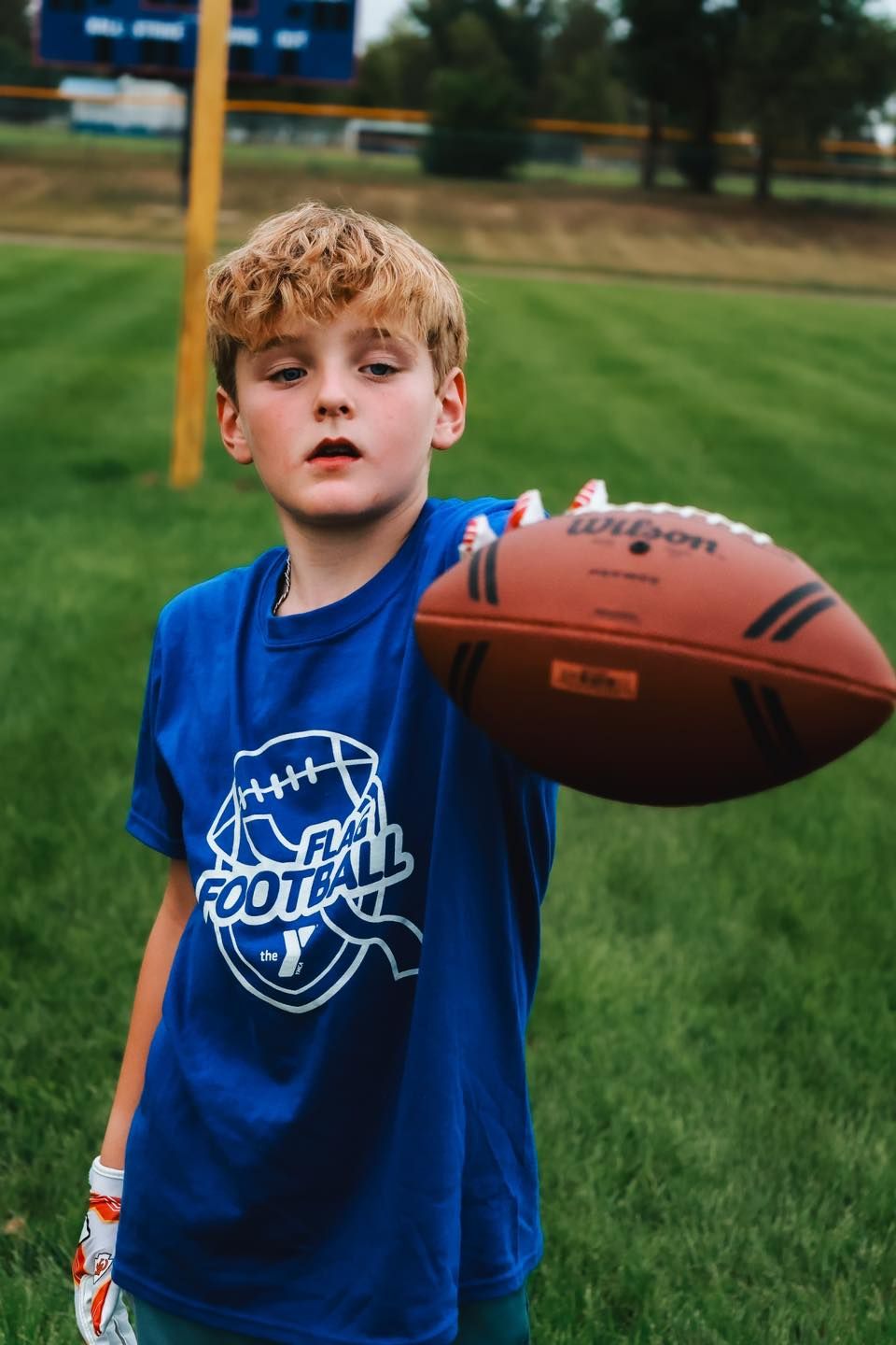 Young boy in blue flag football t-shirt holding a Wilson football on a green grass field. Garrison, ND Photographer